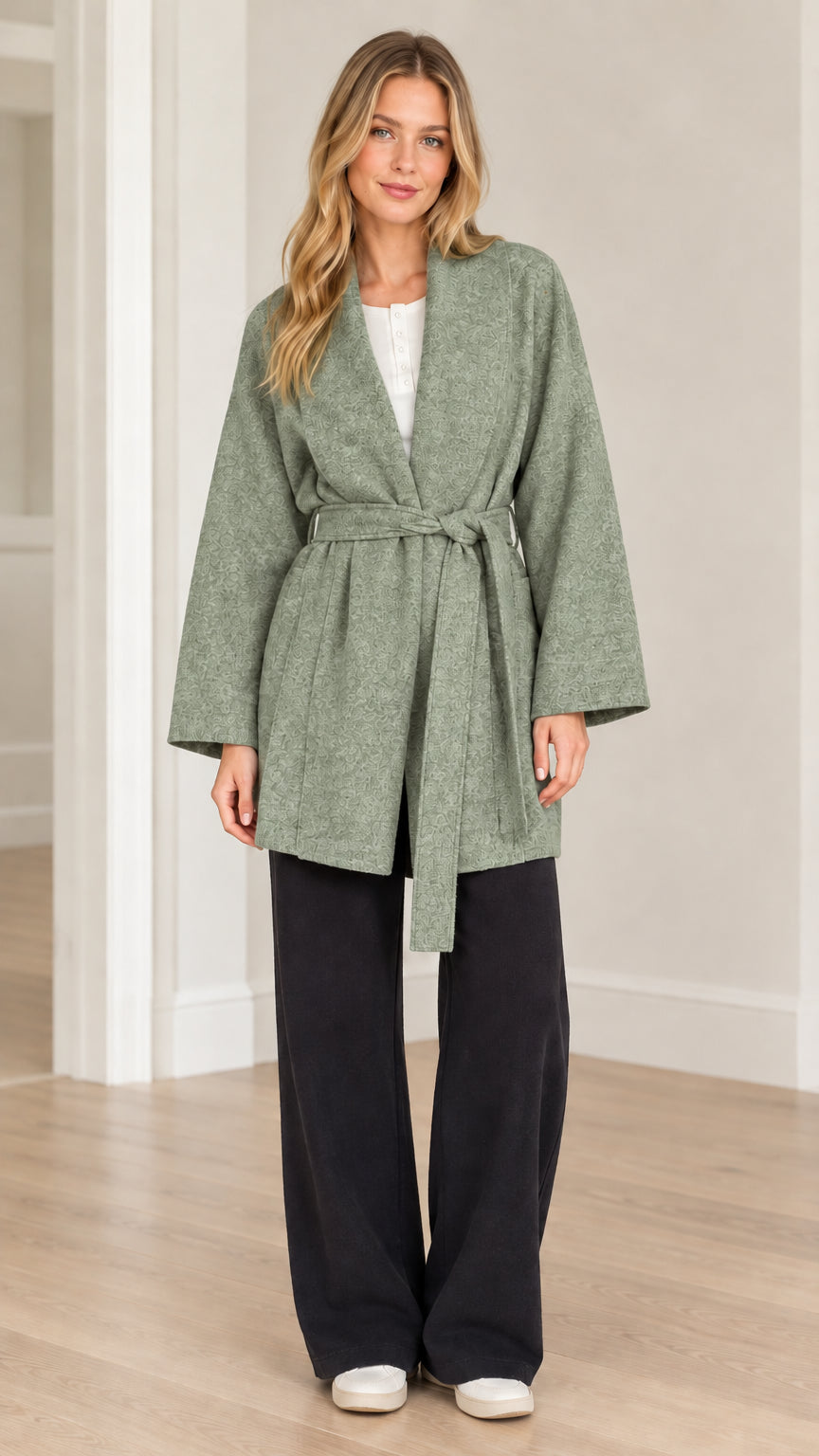 Front view of model wearing sage green textured herringbone belted wrap coat