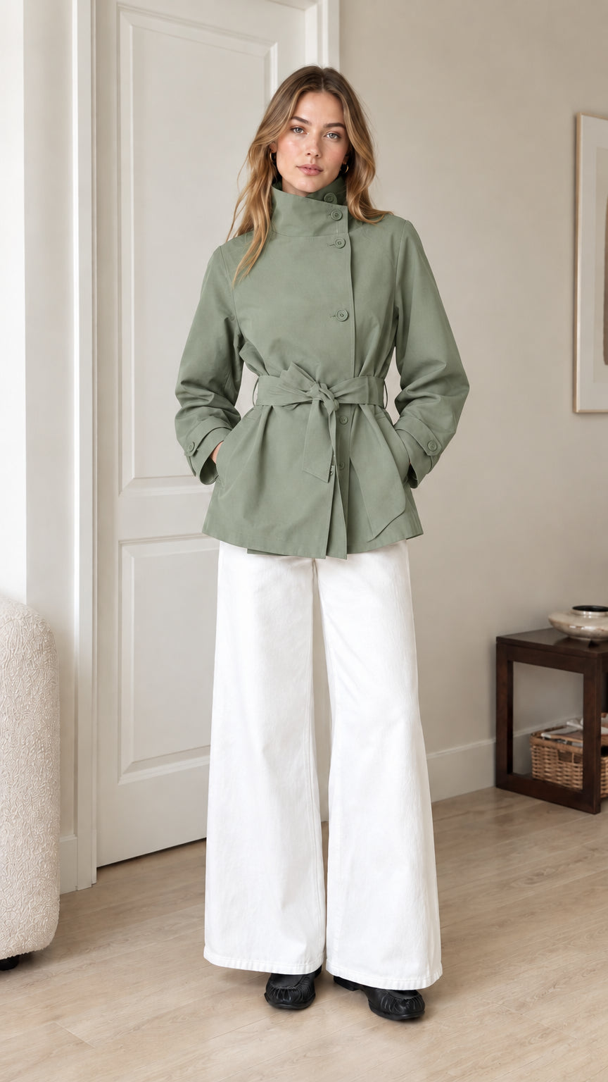 Front view of model wearing sage green belted short trench jacket with white trousers