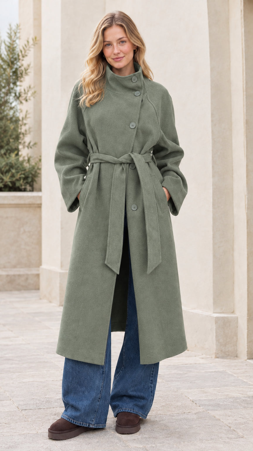 Front full view of woman wearing the sage green asymmetrical high-neck belted overcoat