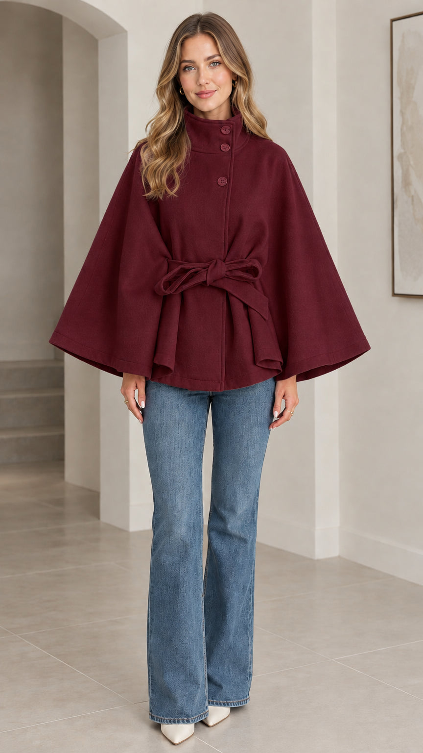 Front view of deep burgundy high neck belted cape coat paired with blue jeans