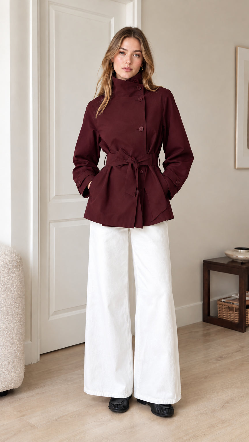 Front view of model wearing burgundy wine red belted short trench jacket with white trousers