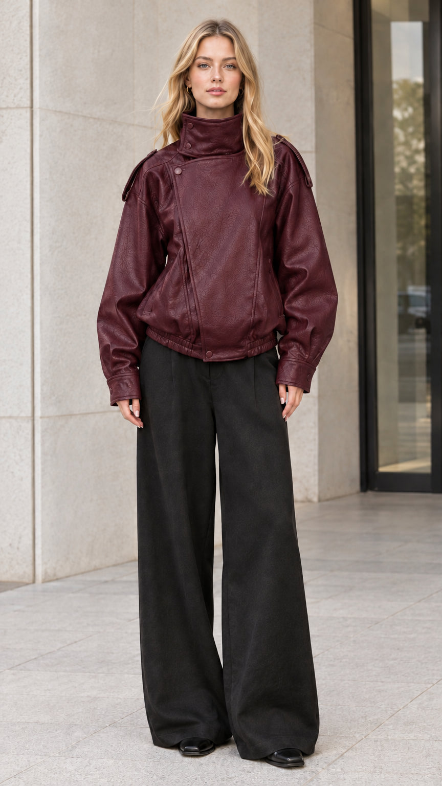 Front full-body view of model wearing rich burgundy faux leather bomber jacket with black trousers