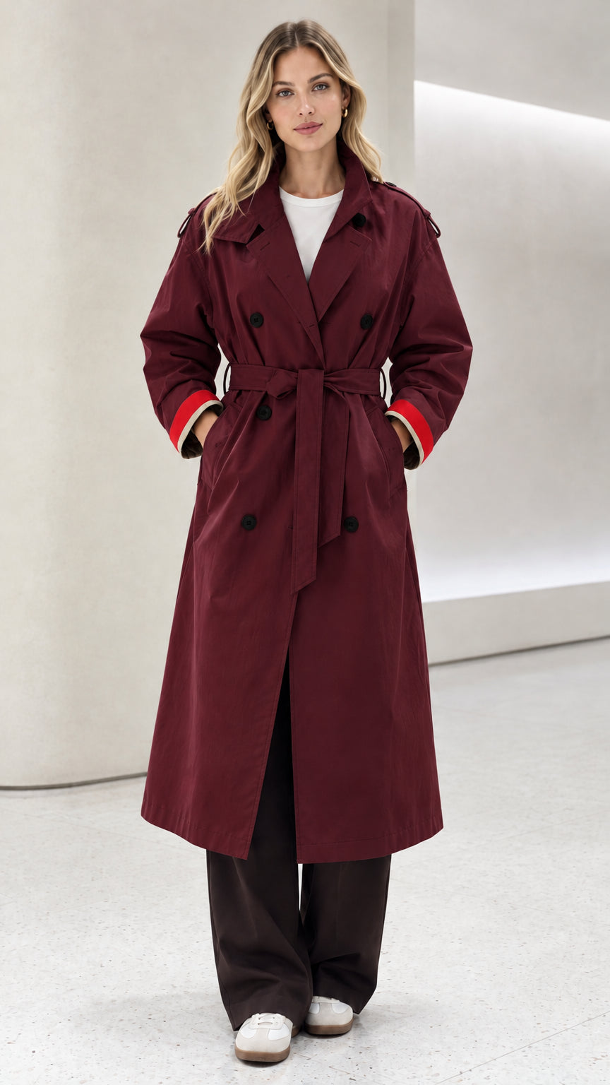 Front view of model wearing deep burgundy double-breasted long trench coat with red cuffs