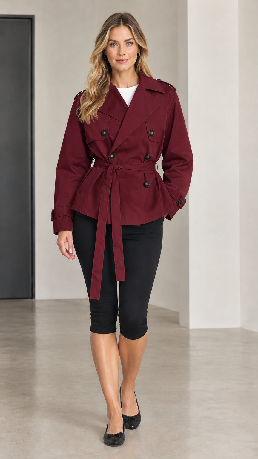 Front view of woman wearing burgundy short double-breasted trench coat with tie belt