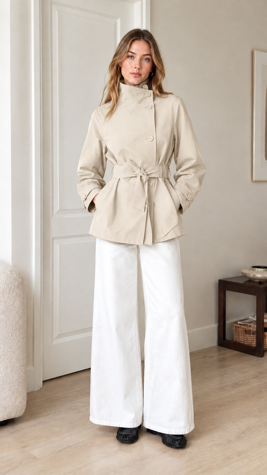 Front view of model wearing beige cream belted short trench jacket with white trousers