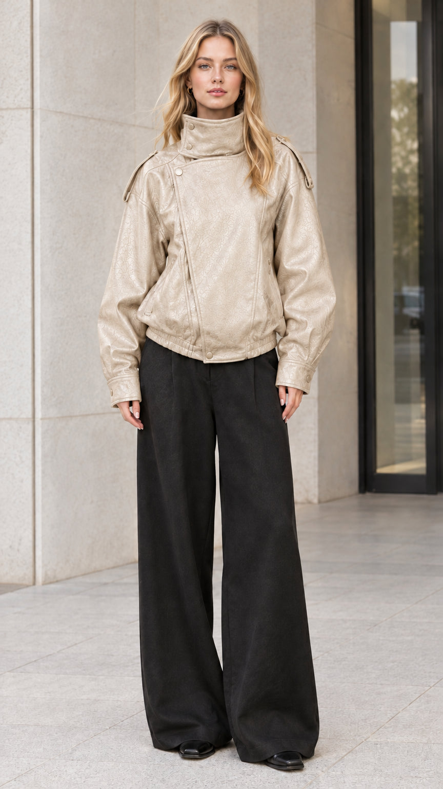 Front full-body view of model wearing beige cream faux leather bomber jacket with black trousers